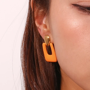 Close-up of gold geometric drop earrings with orange hollow rectangle pendant on model