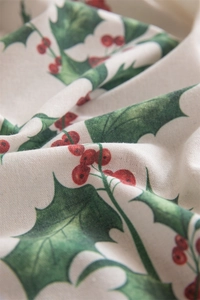 Macro shot of festive holly leaves and red berries printed on textured beige table cloth