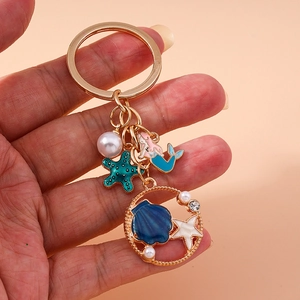 Golden mermaid keychain with starfish, seashells, and pearls on soft pink background