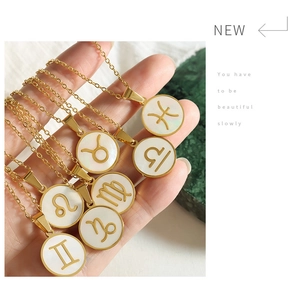 Detail of 12 zodiac necklaces with gold plating and white shell pendants held in hand