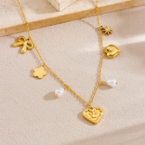 Gold stainless steel necklace with heart crown, flower and pearl pendants on beige texture