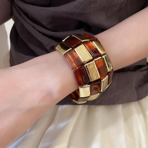 Close-up of wide acrylic bracelet with amber resin segments and golden metal accents