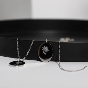 Detailed close-up of oval stainless steel pendants with engraved floral patterns on necklaces