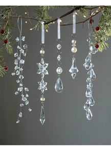 Close-up of clear acrylic snowflake and teardrop ornaments hanging on Christmas tree branches