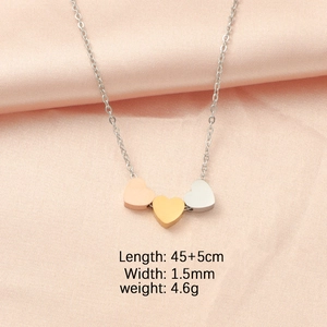 Detailed close-up of triple heart pendants in silver, gold, and rose gold on pink silk