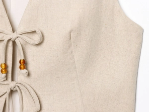Vue macro détaillée du gilet en lin beige avec lacets et perles de couleur ambre