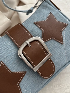 Detail of light blue denim handbag featuring star leather patches and silver square buckle