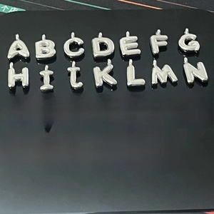 Close-up of 26 silver puffy balloon alphabet charms for DIY jewelry on black background