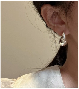 Polished silver S925 sterling silver hollow teardrop earrings shown on a model ear