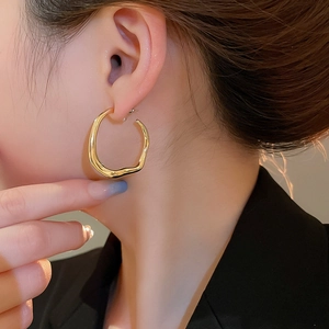 Close-up of elegant gold wave-shaped irregular round hoop earring on female model