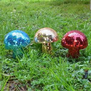 Three reflective mushroom disco balls in blue, gold, and red on a green garden lawn