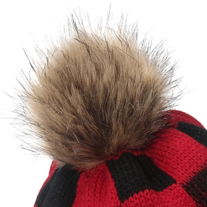 Macro detail of red and black checkered knit hat with soft faux fur pom-pom