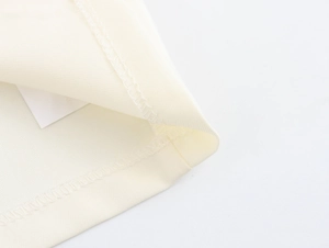 Detailed close-up of woven fabric hem with dense overlock stitching on beige top