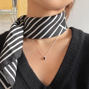 Minimalist silver pendant necklace with black oval stone worn over a black V-neck sweater