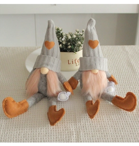 Detail of two knit Christmas gnomes with long pink hair and orange hearts on a white table