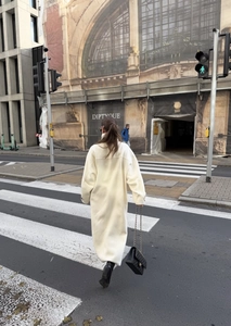 Rear view of a chic long cream wool coat with a relaxed fit during a street scene