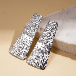 Macro shot of silver geometric square earrings with hammered texture on stone background