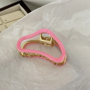 Close-up of a pink wavy metal hair claw clip with golden finish and spring mechanism