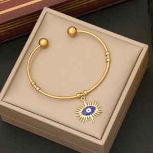 Detail of gold open bangle featuring a blue evil eye charm and ball accents