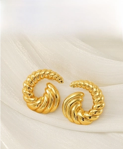 Detail of 18k gold spiral stud earrings featuring a textured metal finish on white silk