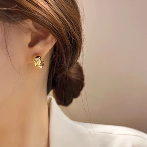 Close-up of elegant C-shaped gold-tone metal earrings worn by a model in soft light