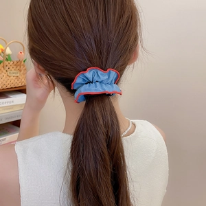 Close-up of blue denim scrunchie with red trim worn on a low ponytail hair style