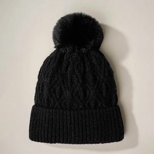 Close-up of black knit beanie with premium pom-pom and thick cable stitch texture