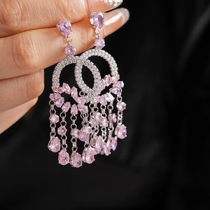 Macro detail of silver tassel earrings featuring pink zircons on a dark background