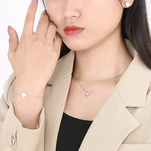 Close-up of heart-shaped silver necklace and bracelet set worn with a beige blazer