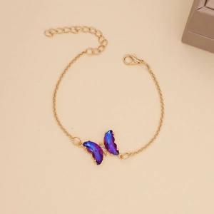 Macro detail of a gold chain necklace with a gradient blue-purple butterfly pendant