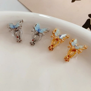 Detail of 18k gold butterfly ear clips with cubic zirconia on white ceramic tray