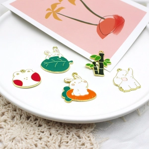 Close-up of cute enamel bunny and elephant charms for DIY jewelry on ceramic tray