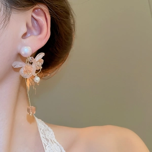 Dettaglio di orecchini a nappa con fiori e perle indossati da una modella su sfondo caldo