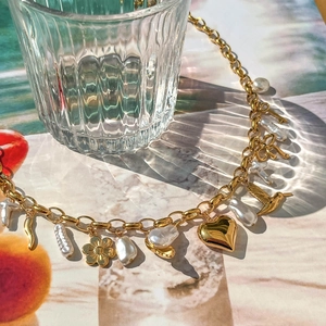 Vue détaillée du collier doré avec perle baroque, pendentifs cœur et colibri
