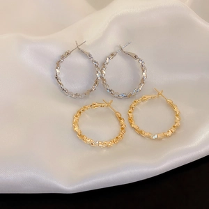 Detailed view of textured gold and silver hoop earrings on elegant white silk fabric