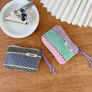 Close-up of woven striped cosmetic pouches on a wooden table with dessert and cutlery