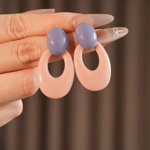 Detail of vintage oval resin earrings in purple and pink tones held by a hand