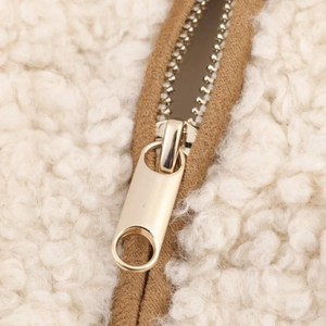 Detailed macro view of smooth gold zipper and soft cream faux shearling fabric texture