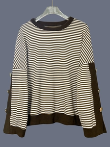 Dettaglio maglione a righe in maglia con bottoni metallici dorati sulle maniche