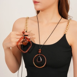 Detail of round and square resin pendants on a black wax cord necklace worn by model