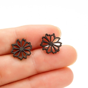 Détail de boucles d'oreilles fleurs noires mates entre les doigts montrant la taille