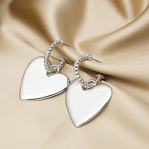 Macro shot of silver heart pendant earrings on elegant champagne satin fabric background