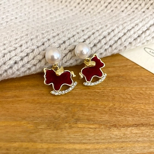 Macro detail of red rocking horse earrings with pearls and rhinestones on soft knit fabric