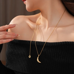 Detail of 18k gold-plated croissant moon pendant necklace on a black knit sweater