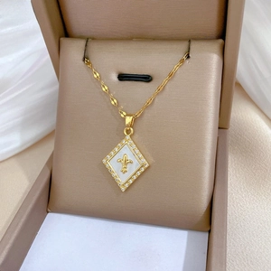 Macro detail of diamond-encrusted fleur-de-lis shell pendant on golden rope chain necklace