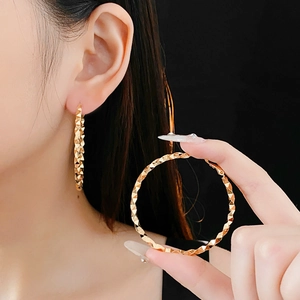 Detailed close-up of large gold hoop earring featuring a diamond-cut textured surface