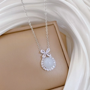 Detail of silver bow necklace with white jade pendant on silk fabric display