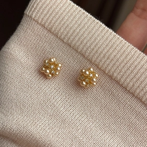 Macro view of gold flower earrings with pearls and rhinestones on beige fabric texture