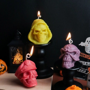 Drei bunte Halloween-Totenkopf-Kerzen in Gelb, Lila und Rot auf schwarzen Kerzenhaltern