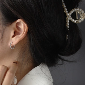 Close-up of twisted silver hoop earring on model showing elegant minimalist metal design